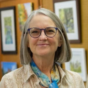Smiling woman in glasses next to her art