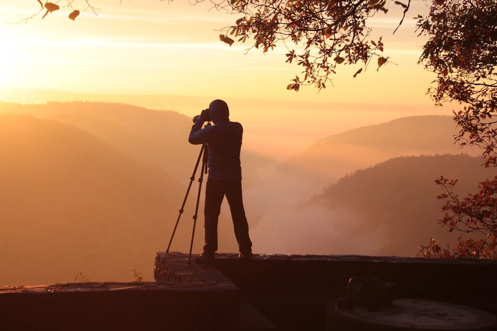 Man with camera on tripod taking a photo of the faraway mountains at sunset.